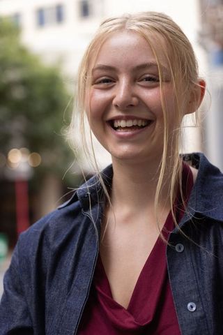 Young woman laughing on urban sidewalk wearing denim jacket and burgundy top, candid portrait