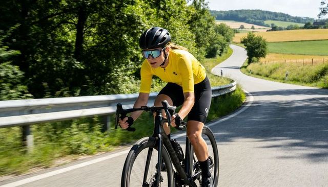Woman cyclist pedaling yellow jersey on winding country road with carbon race bike