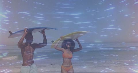 Couple carrying surfboards at breezy beach