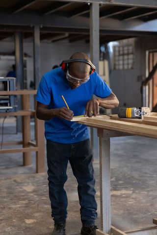 Carpenter measuring and marking long wooden board on workbench with power router