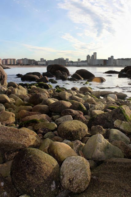 Rocky shoreline with sea in foreground and city buildings in the background. Image can be used for urban nature, coastal scenery, travel destinations, and environmental themes.