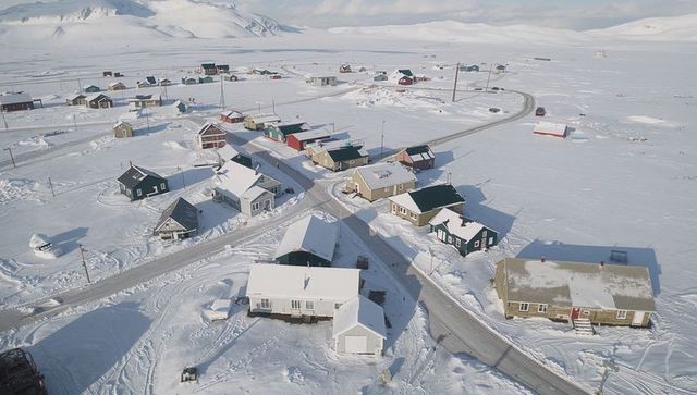 Drone capturing snowy Arctic village with colorful houses on vast frozen plain in sunlight