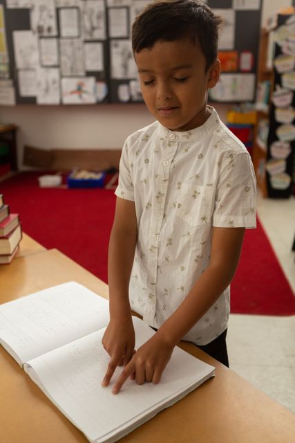 In school, young biracial boy reading a braille book. He has short dark hair, wearing a white patterned shirt, unaltered