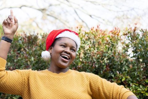 African american woman wearing santa hat and mustard sweater celebrating outdoors