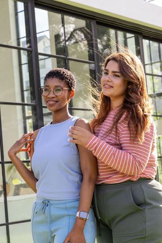 Two female friends standing close outdoors wearing glasses and smartwatch, casual lifestyle