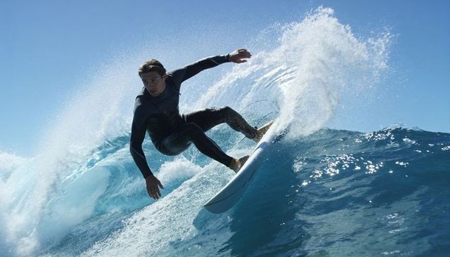 Carving surfer riding crystal blue wave in black full wetsuit on shortboard