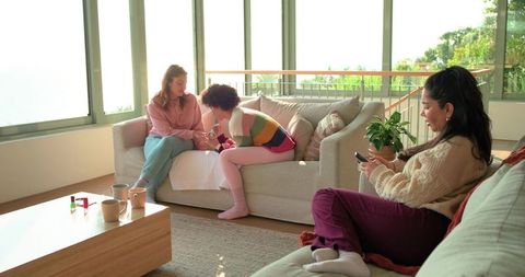 Friends giving at-home manicure in sunlit living room with cozy couches and plants