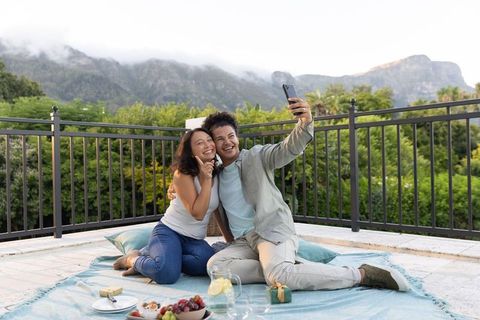 Young couple taking selfie on rooftop picnic with mountain view at sunset
