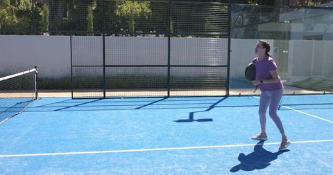 Woman preparing to play padel on vibrant blue court holding paddle