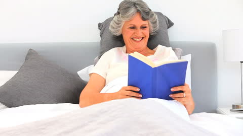 Smiling Elderly Woman Relaxing in Bed with Book