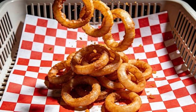 Falling crispy onion rings scattering golden crumbs on red-white checkered liner
