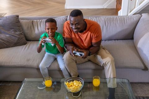 African American father and son playing video games on couch, bonding at home