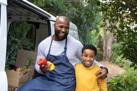 Smiling african american father and son selling fresh peppers from market van outdoors