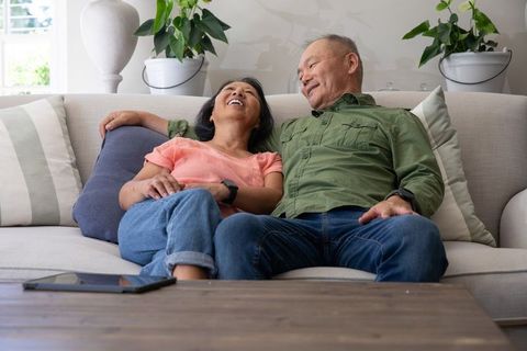 Asian senior couple laughing and relaxing on sofa in cozy neutral living room