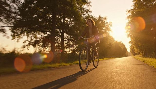 Young man cycling on rural road during golden hour with sun flare and long shadow