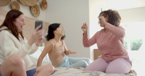 Ladies Sharing Joy and Laughter During a Fun Sleepover on a Cozy Bed