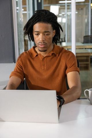 Young professional typing on laptop in modern coworking space, concentrating on task