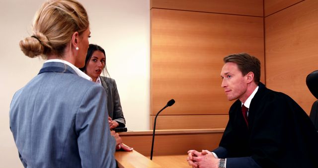 A Caucasian male judge listens intently to a Caucasian female lawyer presenting a case in a courtroom, with copy space. The professional setting underscores the gravity of legal proceedings and the roles of those involved in the justice system.