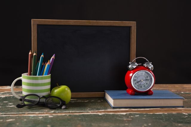 Chalkboard with book, pen holder, apple and spectacles on wooden table