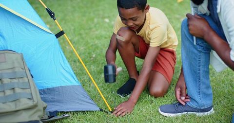 African american father teaching son pitching tent in backyard camping and family bonding