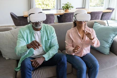 Mature African American couple wearing VR headsets on sofa enjoying virtual reality