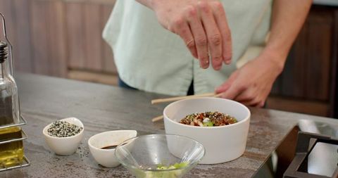 Home cook seasoning healthy rice bowl with fresh ingredients