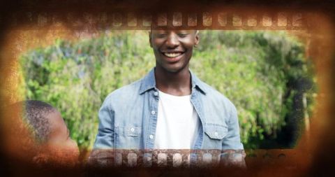 Smiling father in sunlit park wearing denim shirt over white tee vintage filmstrip frame