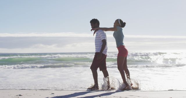 African american man smiling and carrying african american woman piggyback on the beach. healthy outdoor leisure time by the sea.