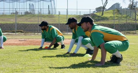 Baseball Infielders Practicing Quick-Reaction Drills in Green and Yellow Uniforms on Grass Field