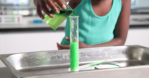 African girl pouring green liquid into graduated cylinder during classroom lab experiment