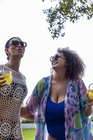 African american friends smiling in backyard wearing summer cover-ups and holding drinks