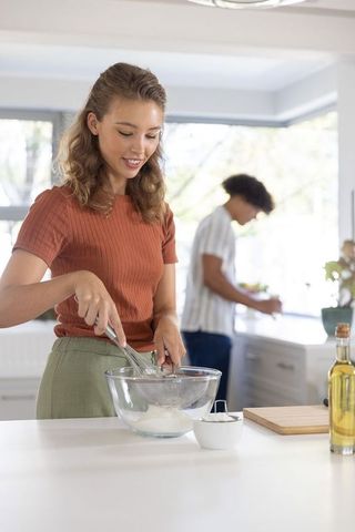 Sunlit home cooking scene with young couple woman whisking batter at kitchen island