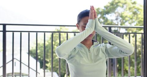 African american woman practicing mindfulness yoga on sunny balcony terrace in zip pullover