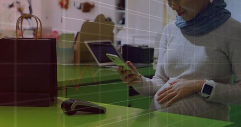 Pregnant woman touching belly while using smartphone for contactless boutique checkout