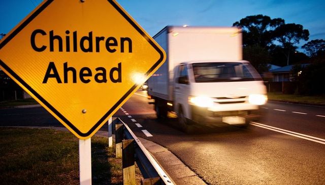 Children ahead warning sign on suburban road with blurred delivery truck at dusk