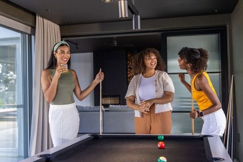 Young diverse women laughing and playing pool with drinks in stylish modern game room