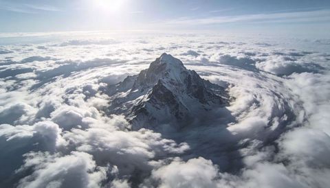 Snow-capped mountain rising through sea of clouds with circular vortex and sunlit horizon panorama
