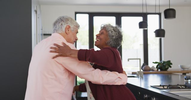 Senior couple enjoying a happy moment in a modern kitchen, sharing a joyful embrace. Ideal for use in advertising for retirement communities, medical care services, lifestyle articles about aging gracefully, and family relationships.