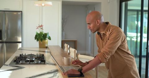 Mature man leaning on kitchen island checking tablet near coffee mug minimalist countertop