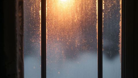 Glowing sunrise light scattering through frosted window panes, icy crystals, condensation