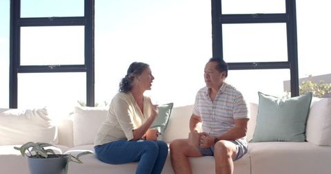 Diverse Couple Relaxing on Sofa with Coffee Mugs in Bright Living Room
