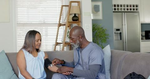 Mature african american caregiver measuring blood pressure of female patient on couch