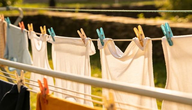 Sunlit white tank tops drying on clothesline with colorful clothespins in backyard garden