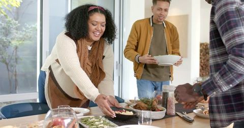 Diverse Friends Serving Homemade Dinner at Sunlit Wooden Dining Table, Casual Gathering
