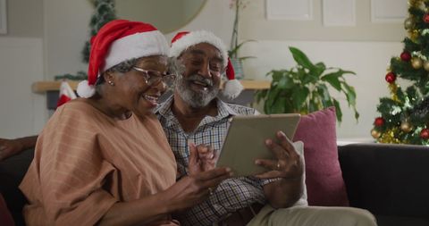 Smiling Senior Couple in Santa Hats Using Tablet at Christmas