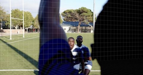 Kneeling rugby players reacting toward camera while silhouetted teammate blocking foreground on fiel
