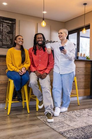 Diverse friends laughing and chatting at cozy coffee shop counter with smartphones