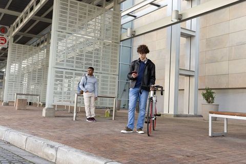 Urban commuters waiting under transit canopy with cyclist holding road bike checking phone