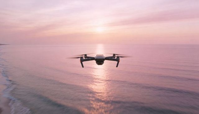 Quadcopter hovering over pastel sunrise ocean capturing sun reflection for aerial film