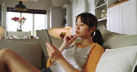 Young Woman Relaxedly Reading on Tablet in Cozy Living Room